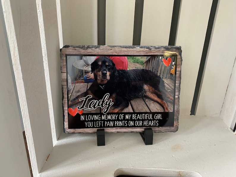May include: A black and brown dog memorial slate with a photo of the dog and the text "Lady" in cursive. The slate also includes the text "In loving memory of my beautiful girl you left paw prints on our hearts".