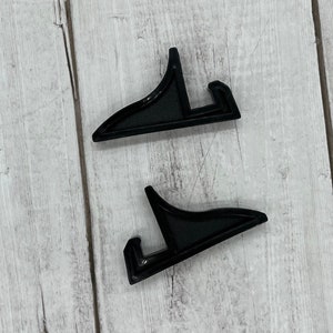 May include: Two black plastic picture frame stands. The stands are shaped like an upside down L.