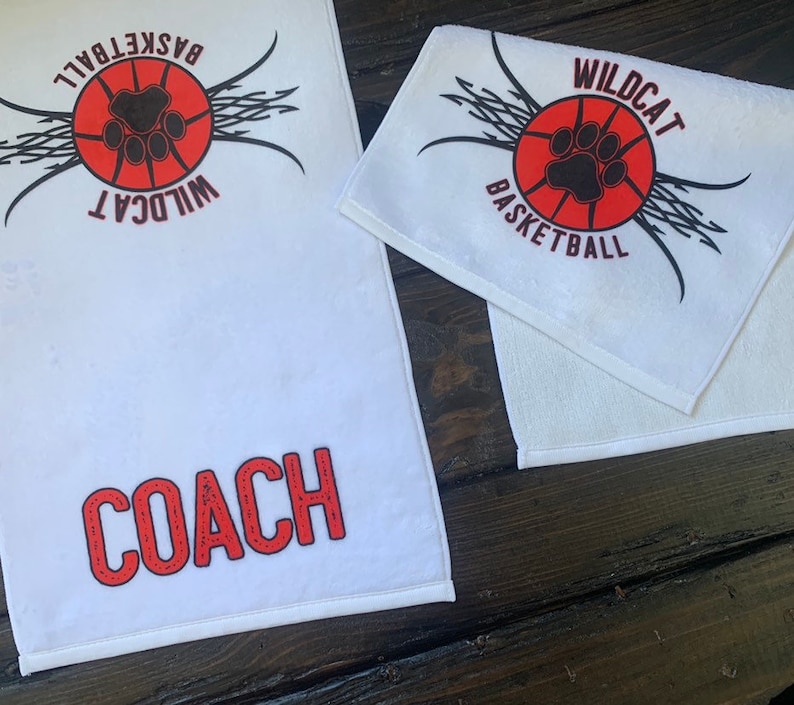 May include: Two white towels with red and black basketball themed designs. One towel says "Wildcat Basketball" and the other says "Wildcat Basketball" and "Coach".