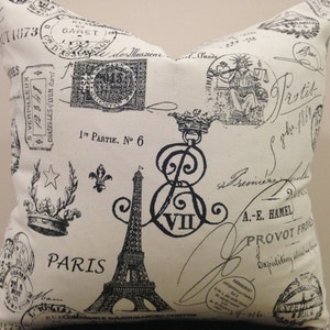 Puede incluir: Una almohada blanca con un estampado en blanco y negro de imágenes de temática parisina, incluyendo la Torre Eiffel, sellos y escritura. El texto "PARIS" está impreso en negro en la almohada.