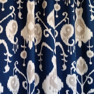 May include: Blue fabric with a white and beige ikat pattern. The fabric has a subtle sheen and a soft texture.