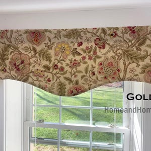 May include: A window valance featuring a beige fabric base with a multi-colored floral pattern in shades of yellow, red, and green. The valance has a scalloped bottom edge and includes the text GOLD HomeandHome printed on the right side.