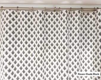 May include: A shower curtain featuring a repeating black botanical leaf pattern on a white background, suspended from a silver metal rod with circular rings. The bottom right corner includes the text Raven-Shade Black in a white box.
