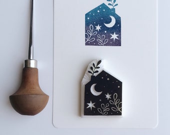 Puede incluir: Un sello de goma blanco con un diseño en blanco y negro de una casa con una luna creciente, estrellas y hojas. El sello está en una tarjeta blanca con un diseño similar en azul y morado.