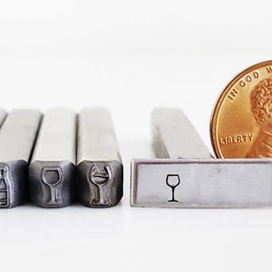 May include: Five metal stamps with different designs, including wine glasses and a wine bottle. The stamps are about the size of a UK penny.