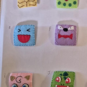 May include: Six square felt patches labelled A, B, E, F, i, and J. Each patch features a unique embroidered character face in various colours including yellow, green, blue, purple, and pink with stitched edges and distinct facial expressions.