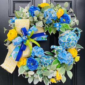 May include: A blue and yellow floral wreath with a teapot and teacup. The wreath is decorated with blue and yellow flowers, green leaves, and a yellow and blue ribbon.