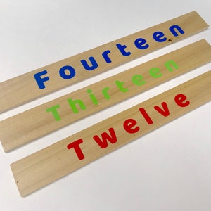 May include: Three wooden blocks with the words "Twelve", "Thirteen", and "Fourteen" painted on them in red, green, and blue paint.