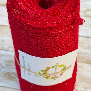 May include: A roll of vibrant red burlap ribbon. The tightly wound fabric is secured with a label that reads "Beautiful Mesh" and is tied with twine. The roll contains 5.5 yards of material.