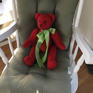 May include: A red teddy bear with a green and white polka dot bow tie sits in a white rocking chair with a green cushion.