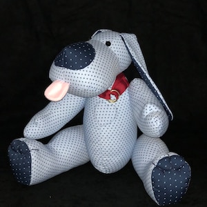 May include: A plush toy dog with a white and blue patterned fabric. The dog has a pink tongue sticking out and is wearing a red collar with a gold buckle.