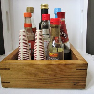 May include: A wooden tray containing a selection of bottles and jars, including soy sauce, vinegar, and other condiments. The tray is made from natural wood and has a rustic appearance.