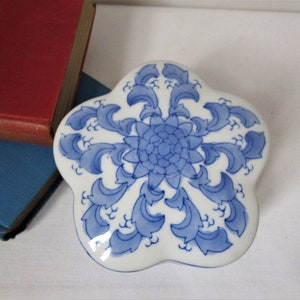 May include: A white porcelain trinket box with a blue and white floral design. The box is shaped like a flower with five petals.