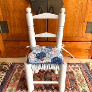 May include: A white wooden chair with a floral patterned cushion. The chair is on a rug with a colourful pattern.