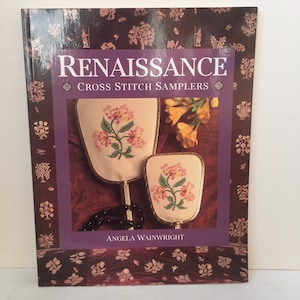 Puede incluir: Un libro titulado "Renaissance Cross Stitch Samplers" de Angela Wainwright. La portada presenta dos abanicos de mano con diseños florales de punto de cruz. El libro tiene un fondo burdeos oscuro con patrones decorativos.