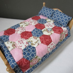 May include: A doll-sized wooden bed with a blue, pink and red patchwork quilt and two blue patterned pillows.