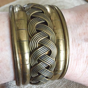 Peut inclure: Un bracelet jonc doré avec un motif tressé. Le bracelet est composé de plusieurs bandes de métal entrelacées.