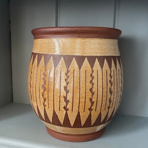 May include: A brown and tan ceramic vase with a geometric pattern. The vase has a wide base and a narrow neck.