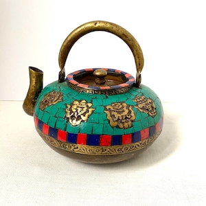 May include: A decorative teapot with a brass handle, spout, and lid. The body is covered in a mosaic of turquoise, red, and blue tiles, with brass embellishments. The teapot has a round shape and a vintage aesthetic.