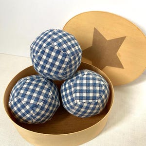 Puede incluir: Tres bolas de tela de guingán azul y blanco en una caja redonda de madera con una estrella en la tapa.