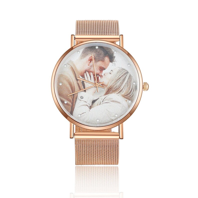 K&ouml;nnte beinhalten: Ros&eacute;goldene Armbanduhr mit einem Mesh-Armband. Das Zifferblatt zeigt ein Foto eines sich k&uuml;ssenden Paares, umgeben von kleinen Kristallen. Die Uhr hat ein klassisches Design mit einem modernen Touch.