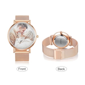 K&ouml;nnte beinhalten: Ros&eacute;goldene Armbanduhr mit einem Mesh-Armband. Das Zifferblatt zeigt ein Foto eines sich k&uuml;ssenden Paares, umgeben von kleinen Kristallen. Die R&uuml;ckseite der Uhr ist sichtbar, mit dem Wort "Raleigh" aufgedruckt.