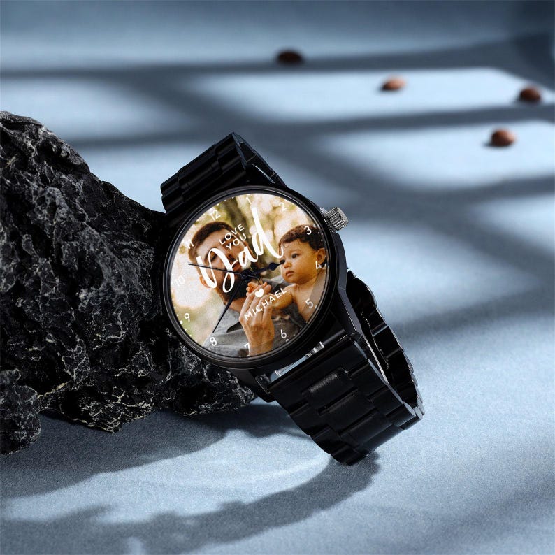 K&ouml;nnte beinhalten: Schwarze Armbanduhr mit einem Foto von Vater und Kind auf dem Zifferblatt. Das Zifferblatt tr&auml;gt die Worte "Love You Dad" und den Namen "Michael". Die Uhr hat ein schwarzes Metallarmband und eine silberne Krone.