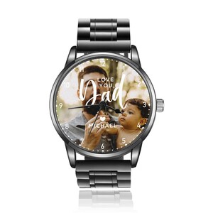 K&ouml;nnte beinhalten: Schwarze Armbanduhr mit einem Foto von Vater und Kind auf dem Zifferblatt. Auf dem Zifferblatt steht in wei&szlig;er Schrift "Love You Dad". Die Uhr hat ein schwarzes Metallarmband und eine silberne Krone.