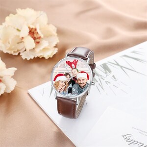 May include: A brown leather watch with a silver case and a custom photo face. The watch face displays a family portrait wearing Santa hats. The watch has a brown leather band.