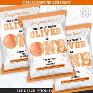 Peut inclure: Trois sacs de cadeaux de f&ecirc;te sur le th&egrave;me du basket-ball. Les sacs sont blancs et orange, avec le texte "it's game time!" et "OUR LITTLE ROOKIE OLIVER is ONE". Chaque sac dit &eacute;galement "THANK YOU FOR COMING!" et a un graphique de basket-ball.