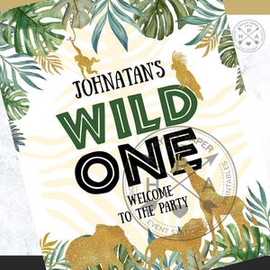 May include: A printable party sign with a jungle theme. The sign says "Johnatan's Wild One" with a green and black font. The background is a white and gold zebra print. There are gold glitter animals, including a giraffe, lion, and elephant.