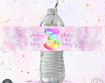 Puede incluir: Etiqueta de botella de agua rosa y blanca con purpurina y un número 3 arcoíris. El texto de la etiqueta dice "Amelia's third birthday".