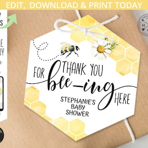 Può includere: Un'etichetta di ringraziamento esagonale bianca con un motivo a nido d'ape giallo e un'illustrazione di un'ape. Il testo recita "Grazie per essere qui" con Baby Shower di Stephanie scritto sotto.
