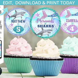 May include: Three cupcake toppers featuring a mermaid and shark theme. The toppers are round and have a glittery background. The text on the toppers reads "Mermaids & Sharks", "Matthew is 5", and "Isabella is 4".