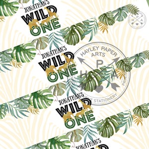 Op de afbeelding: Een printbare banner met een jungle thema. De banner zegt "Jonathan's Wild One" in zwarte tekst met gouden en groene accenten. De banner is versierd met groene bladeren en gouden glitter.