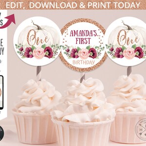 May include: Three cupcake toppers featuring a white pumpkin with a gold glitter background. The toppers have a floral design with pink and burgundy flowers. One topper says "One" in gold glitter, another says "Amanda's First Birthday" in gold glitter, and the third says "One" in gold glitter.