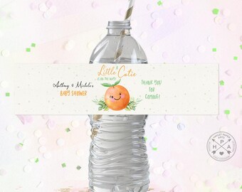 May include: A white and green printable water bottle label with an orange and green illustration of a smiling orange. The label says "A Little Catie is on the way" and "Astlong & Michelle's Baby Shower". The label also says "Thank you for coming!"