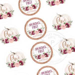 May include: A set of round, white pumpkin-shaped stickers with gold glitter accents. The stickers feature a floral design with pink and burgundy flowers and greenery. The text "One" is written in gold glitter on the pumpkins. The stickers also feature a circle with gold glitter and the text "Amanda's First Birthday".