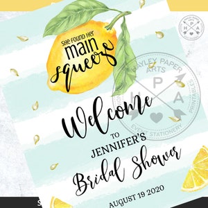May include: A welcome sign for a bridal shower with a lemon illustration and the text "She found her main squeeze". The sign is on a blue and white striped background with the text "Welcome to Jennifer's Bridal Shower August 19, 2020".