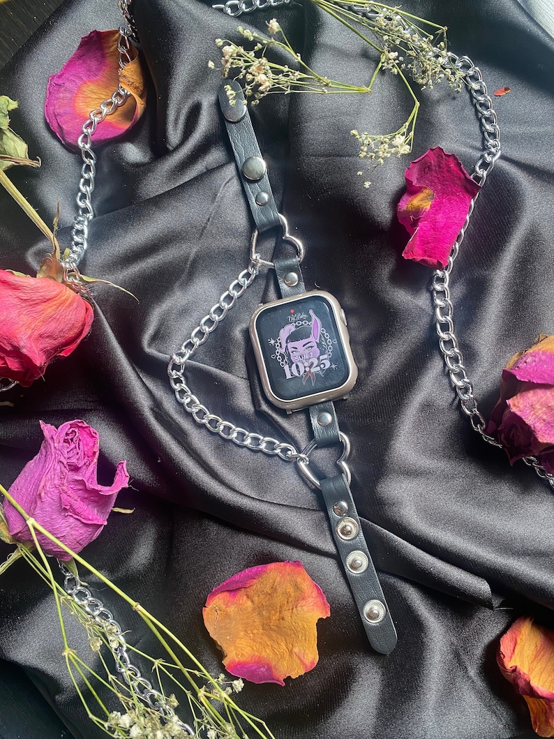 May include: A black leather watch band with silver chain and metal accents. The watch face has a pink and purple cartoon illustration with the text "Lil' Baby 10.25".