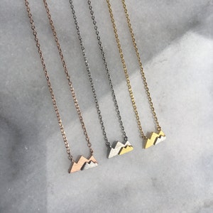 May include: Three delicate gold, silver, and rose gold necklaces with a small mountain pendant. Each necklace features a simple chain style.