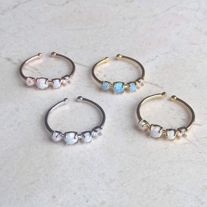 May include: Four dainty rings with three opal stones and a small clear stone accent. The rings are available in silver, gold, and rose gold.