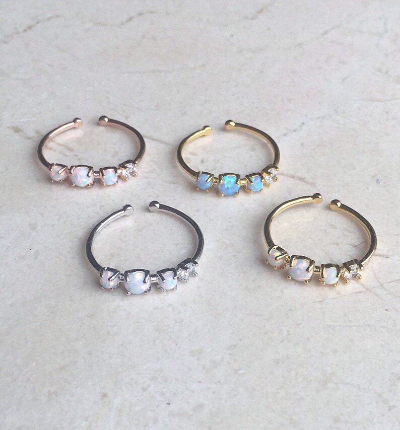 May include: Four dainty rings with three opal stones and a small clear stone accent. The rings are available in silver, gold, and rose gold.
