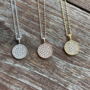 May include: Three silver, rose gold, and gold necklaces with a round pendant encrusted with small white stones.