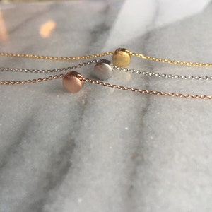 May include: Three delicate necklaces with a single round pendant in rose gold, silver, and gold.