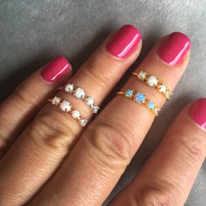 May include: Two gold rings with opal stones. The rings are on a finger with pink nail polish.
