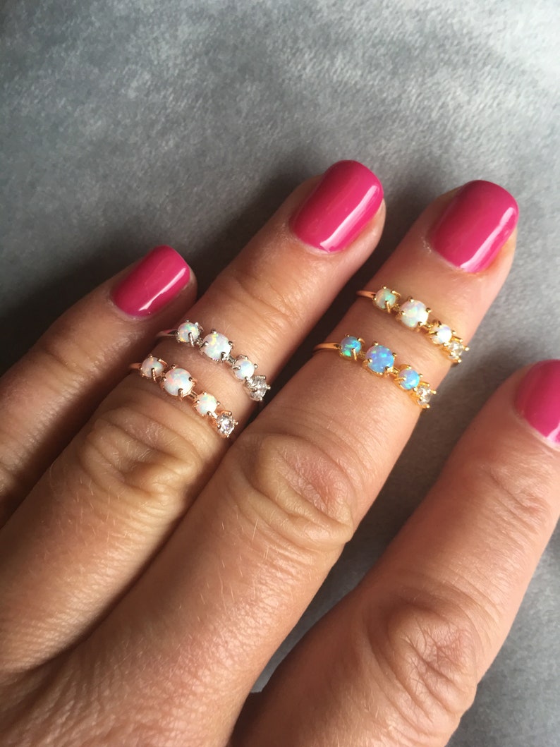 May include: Two gold rings with opal stones. The rings are on a finger with pink nail polish.