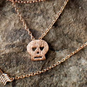 May include: A rose gold necklace with a skull pendant. The skull has heart-shaped eye sockets.
