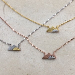 May include: Three delicate necklaces with a mountain range pendant. The pendants are made of gold, rose gold, and silver.