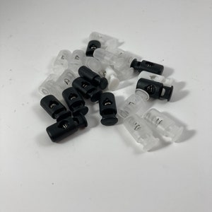 May include: A pile of white and black plastic toggle clasps. The clasps have a spring mechanism and are used for securing cords or straps.
